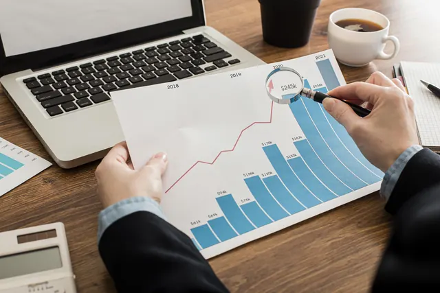 Pessoa analisando gráfico de resultados impresso ao lado de um notebook